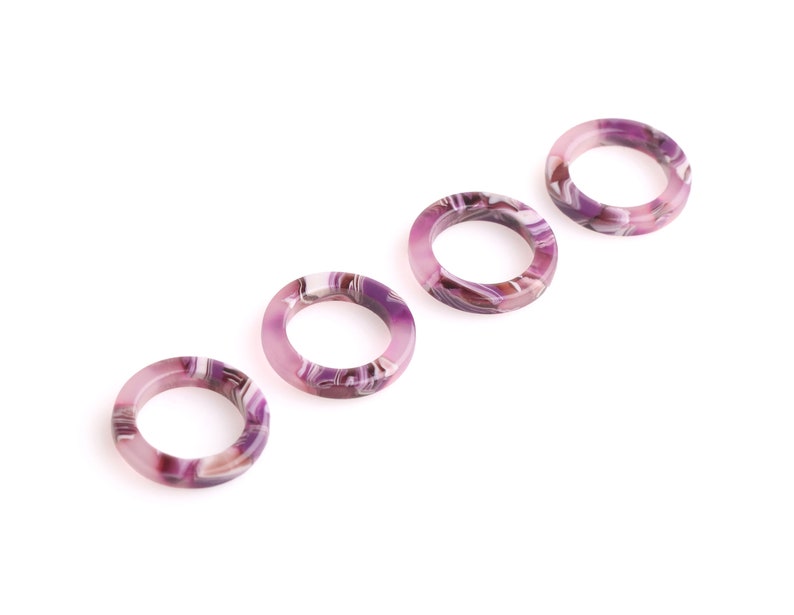 K&ouml;nnte beinhalten: Vier purpurfarbene und wei&szlig;e marmorierte Kunststoffringe. Die Ringe sind in einer Reihe angeordnet, wobei der gr&ouml;&szlig;te Ring links und der kleinste Ring rechts ist.