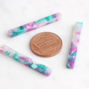 May include: Three colorful, marbled plastic barrettes in shades of pink, green, and white. The barrettes are approximately 2 inches long.