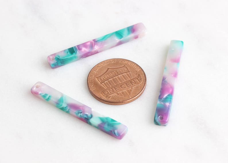 May include: Three colorful, marbled plastic barrettes in shades of pink, green, and white. The barrettes are approximately 2 inches long.