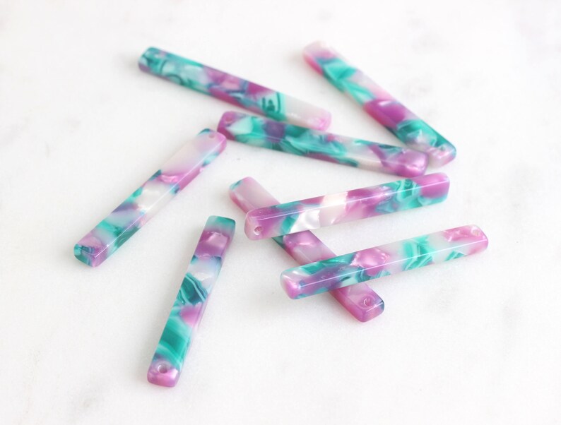 May include: A set of eight colorful, marbled, rectangular acrylic hair clips. The clips are in shades of pink, green, and white.