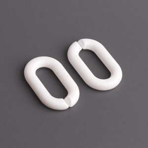 May include: Two white plastic curtain rings, each shaped like an oval with a smaller oval opening in the center.