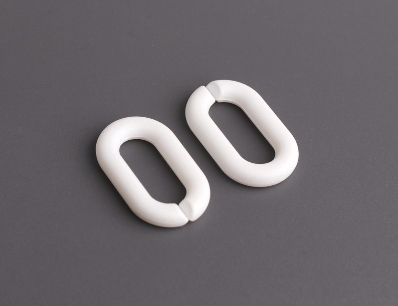 May include: Two white plastic curtain rings, each shaped like an oval with a smaller oval opening in the center.