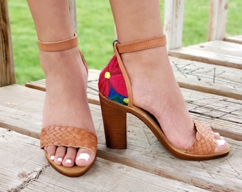 May include: Tan leather heeled sandals with woven straps and a colorful embroidered flower design on the back of the heel.