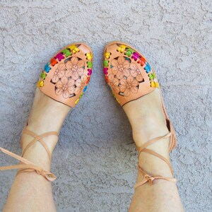 Puede incluir: Un par de sandalias de cuero marr&oacute;n con bordados florales coloridos y ataduras para el tobillo.