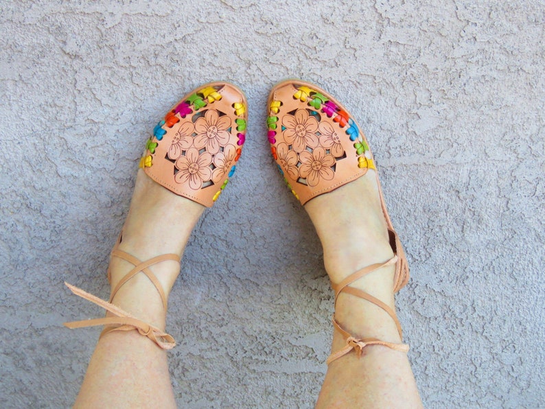 Puede incluir: Un par de sandalias de cuero marr&oacute;n con bordados florales coloridos y ataduras para el tobillo.