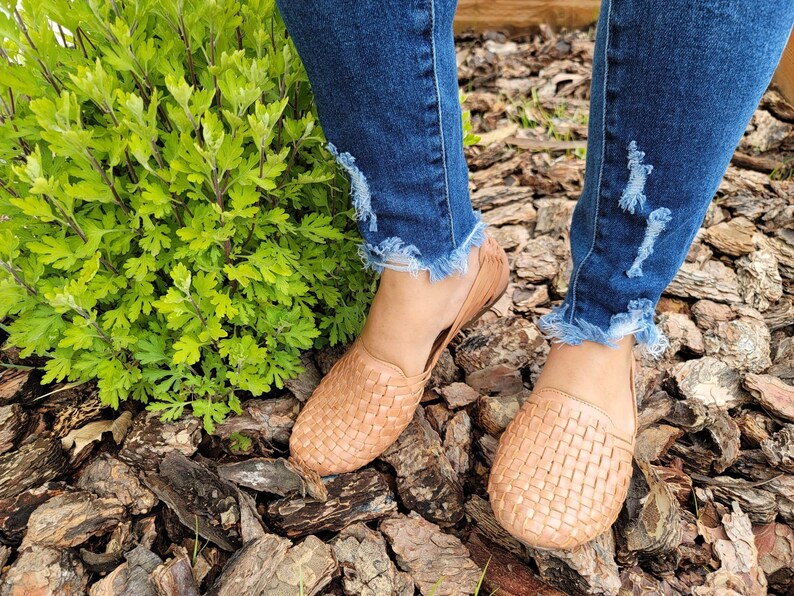 May include: A pair of woven leather flats in a light brown color. The flats are worn by a person wearing distressed denim jeans.