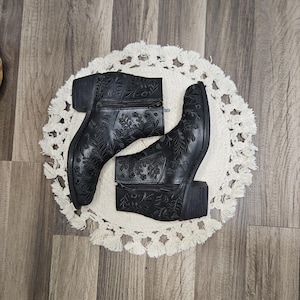 May include: A pair of black ankle boots with floral embroidery. The boots have a block heel and a zipper closure.