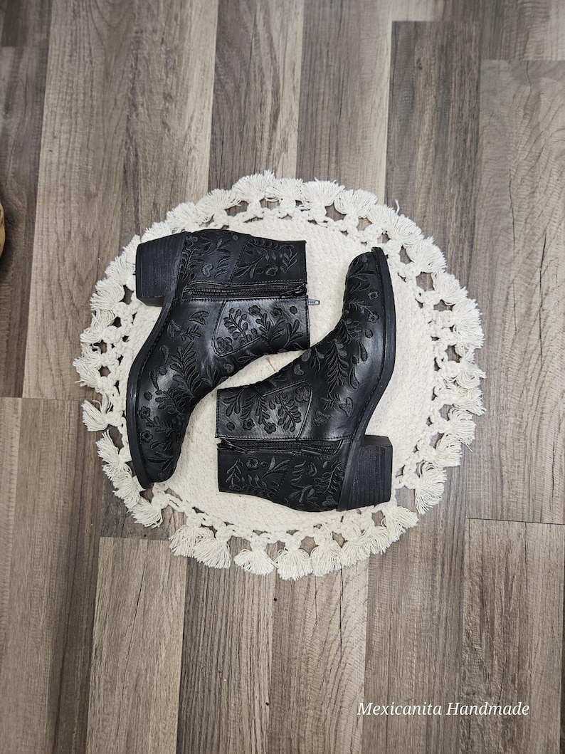 May include: A pair of black ankle boots with floral embroidery. The boots have a block heel and a zipper closure.