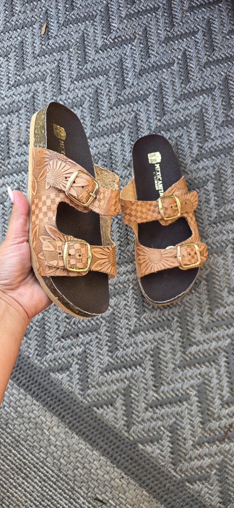 Op de afbeelding: Een paar lichtbruine leren sandalen met twee verstelbare bandjes met goudkleurige gespen. Het leer is voorzien van een reli&euml;f met een zonnebloem- en dambordpatroon. Het voetbed is donkerbruin en de merknaam MEXICANITA is in het wit gedrukt.