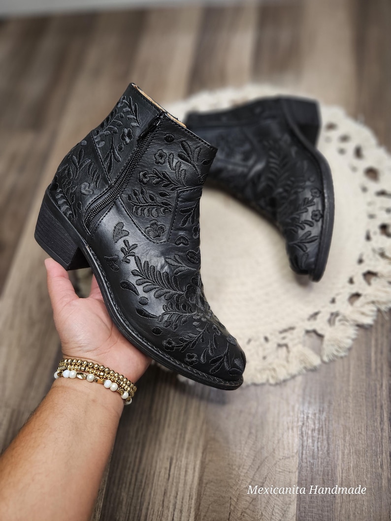 May include: Black ankle boots with a floral embroidery design. The boots have a pointed toe and a low heel.