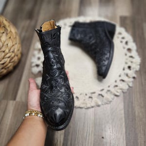 May include: A pair of black leather ankle boots with intricate floral embroidery. The boots have a pointed toe and a low heel.