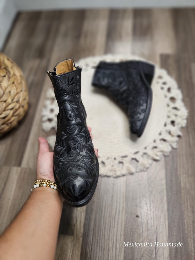 May include: A pair of black leather ankle boots with intricate floral embroidery. The boots have a pointed toe and a low heel.