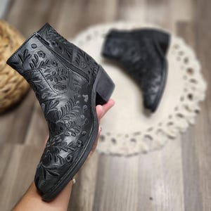 May include: Black ankle boots with floral embroidery. The boots have a zipper on the side and a block heel.