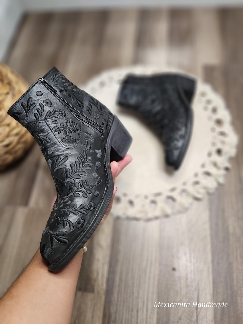 May include: Black ankle boots with floral embroidery. The boots have a zipper on the side and a block heel.