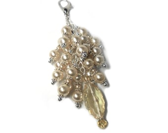 May include: A silver charm with a cluster of cream-colored pearl beads and a clear yellow crystal pendant.