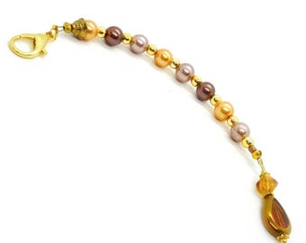 May include: A decorative beaded chain featuring alternating round peach, brown, and mauve pearls interspersed with small gold-toned metal beads. The chain terminates with a gold-toned lobster clasp at one end and a faceted amber-colored teardrop pendant.