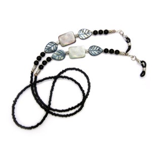 May include: Black beaded eyeglass chain with silver leaf and shell accents. The chain is made of small black beads and has two silver leaf charms and two rectangular shell charms.