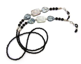 May include: Black beaded eyeglass chain with silver leaf and shell accents. The chain is made of small black beads and has two silver leaf charms and two rectangular shell charms.