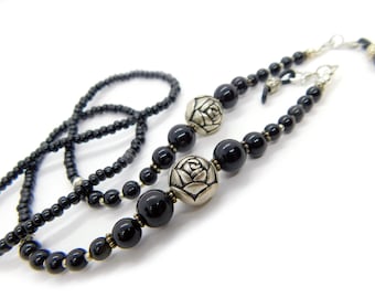 May include: A beaded eyewear chain featuring smooth black spherical beads interspersed with metallic silver-toned beads shaped like roses. The chain includes small silver-colored spacers and terminates with clear rubber loops for attaching to glasses frames.