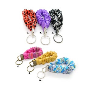 May include: Six colorful fabric keychains with metal rings. The keychains are in various patterns, including leopard print, floral, and geometric designs. The keychains are numbered 1 through 6.