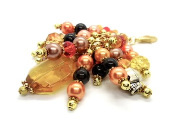 May include: A beaded charm with a variety of colors, including peach, gold, black, and red. The charm features a large, clear, faceted crystal.