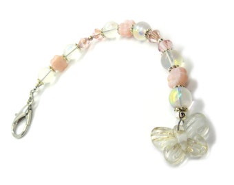 May include: A white and pink beaded keychain with a clear butterfly charm. The keychain has a silver clasp.