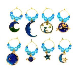 May include: Set of eight blue and gold wine glass charms with celestial designs, including moons, stars, planets, and a cat. Each charm is attached to a gold ring with blue crystal beads.