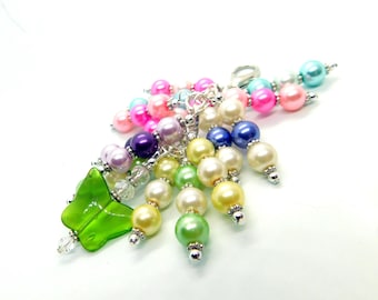 May include: A colorful beaded charm with a green butterfly pendant. The charm features a variety of pastel beads, including pink, blue, green, and white.