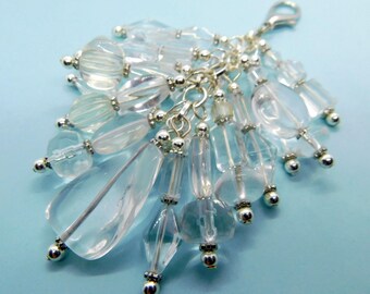 May include: A clear crystal charm with a silver clasp and chain. The charm is made of various clear beads and crystals in different shapes and sizes, including teardrops and ovals. The beads are strung together with silver-colored metal findings.