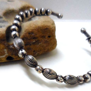 May include: A silver bracelet with alternating round and oval beads. The oval beads have a textured, ribbed design.