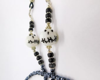 May include: Eyeglass chain featuring white, round beads with black stitched-mouth designs, interspersed with black and silver beads. The chain has a silver-tone metal clasp and a dark blue beaded section.