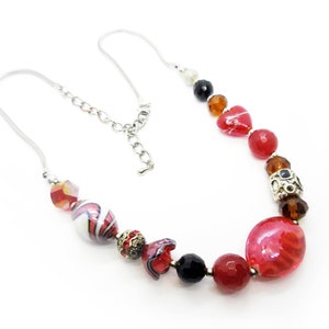 May include: A red, white, and black beaded necklace with a silver chain and clasp. The beads are various shapes and sizes, including hearts, ovals, and round beads.