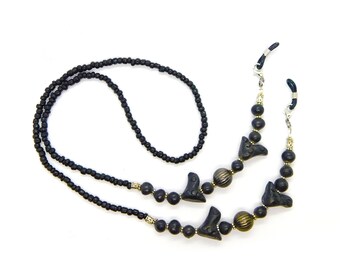 May include: Black beaded eyeglass chain with black and gold accents. The chain has two small black bird-shaped charms and two silver clasps.