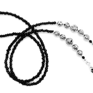 May include: Black beaded eyeglass chain with silver metal beads. The chain has two loops at the ends for attaching to glasses.