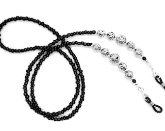 May include: Black beaded eyeglass chain with silver metal beads. The chain has two loops at the ends for attaching to glasses.