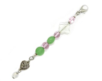 May include: A beaded charm with a silver clasp and heart-shaped charm. The charm features green, pink, and clear beads, along with a clear, flower-shaped bead. The heart charm has a decorative swirl design.