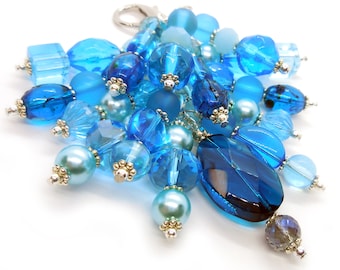 May include: A blue and teal beaded keychain with a silver charm. The keychain features a variety of different shaped beads, including round, oval, and square beads.