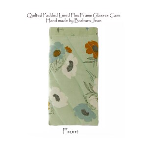 May include: A quilted glasses case with a floral pattern in shades of white, blue, and orange on a light green background. The case is padded and lined, with a flex frame. The text "Quilted Padded Lined Flex Frame Glasses Case Hand made by Barbara Jean" is visible.