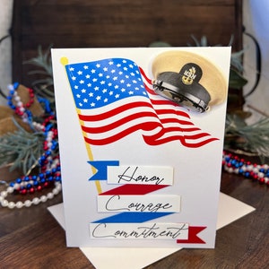 May include: A patriotic greeting card featuring an American flag and a navy cap. The card includes the words "Honor, Courage, Commitment" on banners. The design uses red, white, and blue colors.