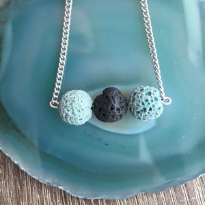 May include: A silver chain necklace with three lava rock beads. Two of the beads are light blue and one is black.