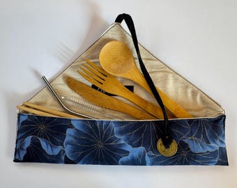 May include: A reusable bamboo utensil set includes a spoon, fork, knife, chopsticks, and a straw with a cleaning brush. The utensils are stored in a navy blue floral patterned carrying case with a black strap and a gold coin charm.