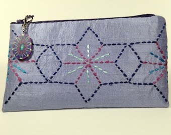 May include: A lavender silk zippered pouch with a decorative button and embroidered starburst designs in shades of blue, pink, and green.