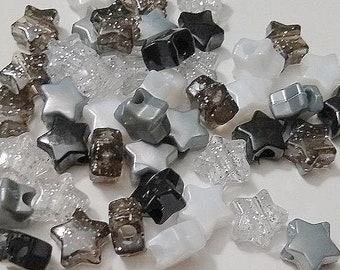 May include: A pile of star-shaped beads in white, black, gray, and brown colors. The beads are made of plastic and have a shiny finish.