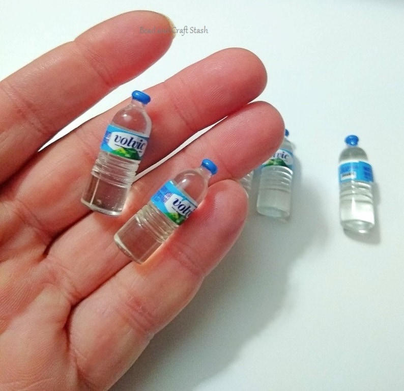 Puede incluir: Cuatro botellas de agua de pl&aacute;stico en miniatura con tapas azules y etiquetas que dicen "Volvic".