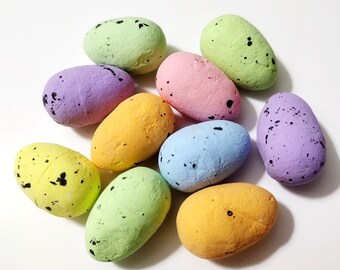 May include: A collection of ten colorful, speckled Easter eggs in various pastel shades, including green, purple, yellow, pink, and blue. Each egg has a textured surface and is dotted with black speckles. The eggs are arranged on a white background.