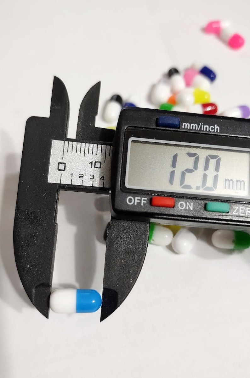 May include: A blue and white capsule pill being measured with a digital caliper. The caliper reads 12.0 mm.