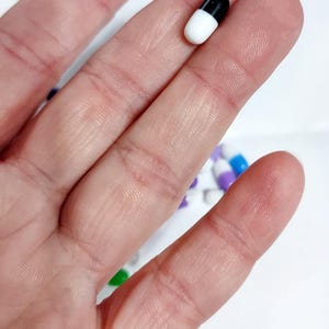 May include: A white and black capsule pill held between two fingers.