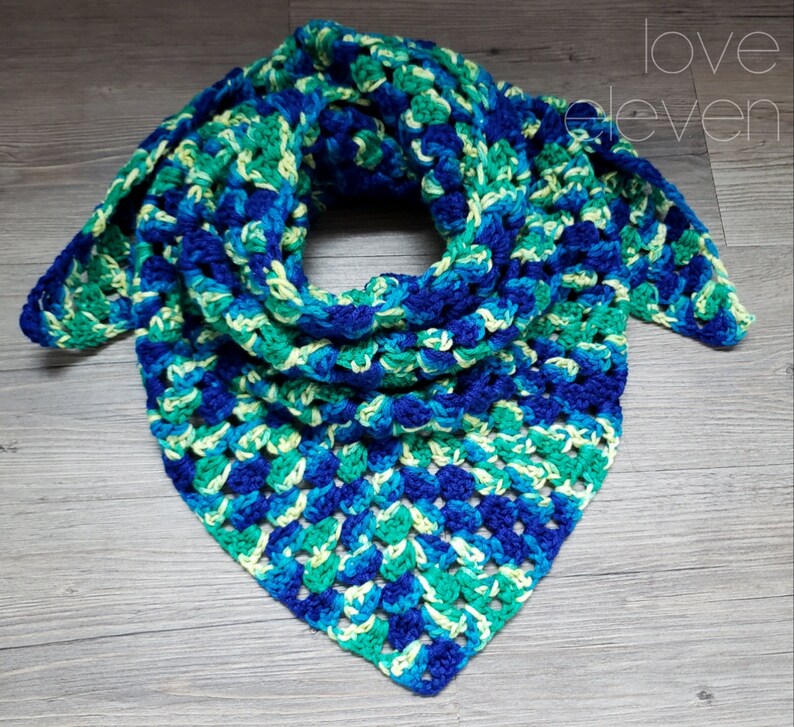 Op de afbeelding: Een driehoekige gehaakte sjaal in tinten blauw, groen en geel. De sjaal is gemaakt met een granny square steekpatroon.