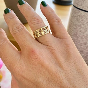 Puede incluir: Un anillo dorado con un diseño de eslabones de cadena. El anillo, usado en un dedo, muestra un patrón intrincado y un acabado pulido. El diseño incorpora una serie de eslabones interconectados, formando una banda continua. Un accesorio elegante.