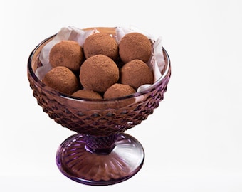 May include: A purple glass bowl filled with chocolate truffles. The bowl has a decorative diamond pattern and a pedestal base.